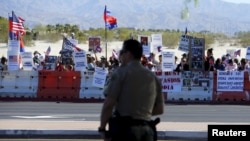 មន្ត្រី​ប៉ូលិស​ម្នាក់​កំពុង​ឈរ​មើល​ក្រុម​បាតុករ​ដែល​នៅ​ម្ខាង​ផ្លូវ​ឆ្ពោះ​ទៅ​កាន់​រមណីយដ្ឋាន ​Sunnylands ជាកន្លែង​ដែល​ប្រធានាធិបតី​ បារ៉ាក់​ អូបាម៉ា​ ទទួល​ស្វាគមន៍​មេដឹកនាំ អាស៊ាន​ទាំង​១០ កាល​ពី​ថ្ងៃទី​១៥ ខែ​កុម្ភៈ​ ឆ្នាំ២០១៦។