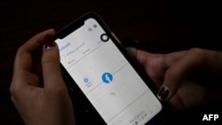 ရန်ကုန်မြို့မှာ မိုဘိုင်းဖုန်းကနေ ဖေ့စ်ဘုတ်အသုံးပြုနေသူတဦး။ (ဖေော်ဝါရီ ၄၊ ၂၀၂၁။ ဓာတ်ပုံ - STR / AFP)