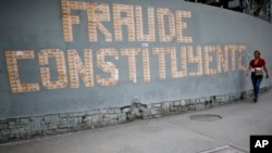 A pedestrian walks next to a message on a wall formed with Venezuelan currency that reads in Spanish: “The Constituent Assembly is a fraud” in Caracas, Venezuela, July 31, 2017.