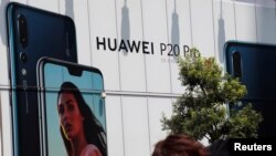 មនុស្សម្នា​ដើរ​កាត់​ផ្ទាំង​ពាណិជ្ជកម្ម​សម្រាប់​ក្រុមហ៊ុន Huawei នៅ​ខាង​ក្រៅ​ហាង​លក់​គ្រឿង​អេឡិចត្រូនិច នៅ​ក្នុង​ក្រុង​តូក្យូ ប្រទេស​ជប៉ុន កាលពី​ថ្ងៃទី៦ ខែសីហា ឆ្នាំ២០១៨។