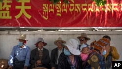 资料照片：在西藏拉萨一处寺庙附近，藏民在用汉语和藏语写成的政府宣传横幅下休息。(2021年6月3日)