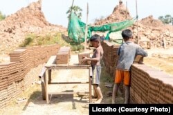 ក្មេងប្រុសពីរនាក់កំពុង​លើ​ដុំ​ឥដ្ឋ​ដាក់​លើ​រទេះ​ឈើមួយ នៅ​សិប្បកម្មឡឥដ្ឋមួយកន្លែងនៅប្រទេស​កម្ពុជា។ (រូបថតដោយ Licadho)