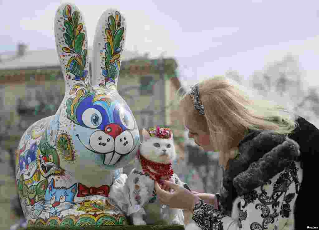 A woman dresses her cat before taking pictures near a painted Easter Bunny, displayed in a square as part of the upcoming Orthodox Easter celebration, in central Kyiv, Ukraine.