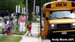 In Wisconsin, teachers watch as pre-school children get on their school bus. (AP Photo/Andy Manis)