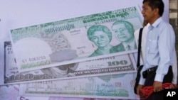 រូបឯកសារ៖ បុរស​កម្ពុជា​ម្នាក់​ឈរ​នៅ​ក្បែរ​ផ្ទាំង​បដា​ដែល​មាន​បង្ហាញ​រូបិយវត្ថុ​ផ្សេង​នៅ​ក្នុង​កម្មវិធី​សម្ពោធន៍​ទីផ្សារ​ភាគហ៊ុន​កម្ពុជា​នៅ​ទីក្រុង​ភ្នំពេញ។ (AP Photo/ហេង ស៊ីនិត) 