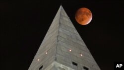 FILE - The supermoon passes behind the top of Washington Monument during a lunar eclipse on Sept. 27, 2015. People in many parts of North and South America will be able to see a total lunar eclipse Sunday night, Jan. 20, 2019 and early Monday morning.