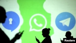 FILE - Silhouettes of mobile users are seen next to logos of social media apps Signal, Whatsapp and Telegram projected on a screen in this picture illustration.