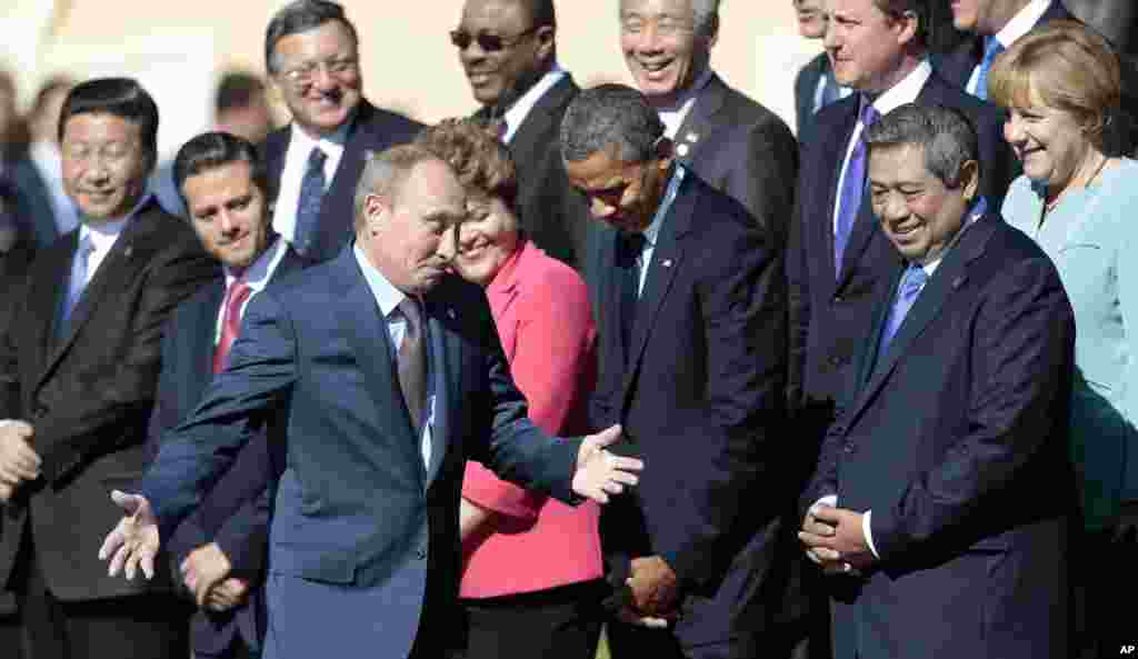 Russia's President Vladimir Putin, center foreground, gestures as he walks by U.S. President Barack Obama, front row second right, as he takes his place at a group photo outside of the Konstantin Palace in St. Petersburg, Russia, Sept. 6, 2013. 