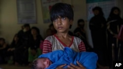Rohingya Muslim girl Afeefa Bebi, who recently crossed over from Myanmar into Bangladesh, holds her few-hours-old brother as doctors check her mother Yasmeen Ara at a community hospital in Kutupalong refugee camp, Bangladesh, Wednesday, Sept. 13, 2017. The family crossed into Bangladesh on Sept. 3. Recent violence in Myanmar has driven hundreds of thousands of Rohingya Muslims to seek refuge across the border in Bangladesh. But Rohingya have been fleeing persecution in Buddhist-majority Myanmar for decades, and many who have made it to safety in other countries still face a precarious existence. (AP Photo/Dar Yasin)
