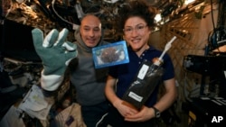 In this photo made available by U.S. astronaut Christina Koch via Twitter on Dec. 26, 2019, she and Italian astronaut Luca Parmitano pose for a photo with a cookie baked on the International Space Station. Researchers want to inspect the handful of…