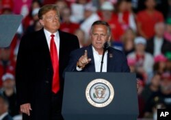 President Donald Trump listens as Rep. Mike Bost, R-Ill., speaks during a rally at Southern Illinois Airport, Oct. 27, 2018, in Murphysboro, Ill.