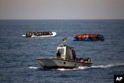 FILE - A Libyan Coast Guard ship sails past two rubber boats packed with migrants and refugees in the Mediterranean Sea, about 18 miles north of Sabratha, Libya, June 15, 2017.