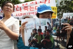 FILE - An unidentified North Korean defector holds a picture of nine North Korean defectors who were flown home as she cries during a rally protesting Laos' repatriation of them, in Seoul, South Korea, June 5, 2013.