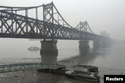 FILE - Trucks move across the bridge linking North Korea with the Chinese border city of Dandong, March 3, 2016. China has banned imports of gold and rare earths from North Korea as well as exports to the country of jet fuel and other oil products.