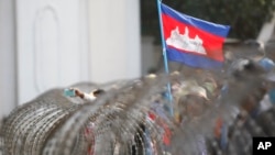 រូបឯកសារ៖ ទង់ជាតិខ្មេរត្រូវបានដោតលើរបងលួសដែលប៉ូលិសបានដាក់បិទច្រកចូលអគាររបស់ទីស្តីការគណៈរដ្ឋមន្ត្រី ក្នុងអំឡុងពេលបាតុកម្មមួយដែលធ្វើឡើងដោយកម្មកររោងចក្រទាមទារការដំឡើងប្រាក់ឈ្នួល នៅរាជធានីភ្នំពេញ កាលពីថ្ងៃទី ៣០ ខែធ្នូ ឆ្នាំ ២០១៣។