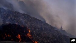 FILE - A person picks through trash for reusable items as a fire rages at the Bhalswa landfill in New Delhi, April 27, 2022. (AP Photo/Manish Swarup, File)