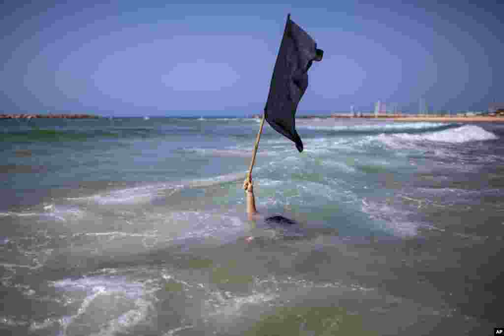 A man waves a black flag in the water during a protest against government's decision to close beaches during the three-week nationwide lockdown due to the coronavirus pandemic,in Tel Aviv, Israel, Sept 19, 2020.