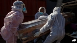 Funeral home workers in protective suits carry the coffin of a woman who died from COVID-19 into a hearse in Katlehong, near Johannesburg, South Africa, 
