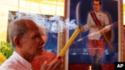 Cambodian man holds the burned incense sticks in front of a painted photo of a Kampuchea Krom Hero, Son Kuy, right, at a ceremony in Phnom, file photo. 