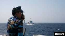 FILE - An officer of the Vietnamese coast guard officer speaks on a radio as he monitors a Chinese vessel (top) in the South China Sea, about 210 km (130 miles) off Vietnam's shore.
