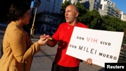 Claudio Mariani, de 59 años, diagnosticado como VIH positivo en 1993, sostiene un cartel que dice "con VIH vivo, con Milei muero", mientras entrega un condón gratis a una mujer, en Buenos Aires, Argentina, el 29 de noviembre de 2024. 