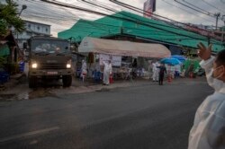 មន្ត្រីប៉ូលិសថៃកំពុងជម្លៀសពលករចំណាកស្រុកនិងសមាជិកគ្រួសារ ទៅកាន់កន្លែងធ្វើតេស្តរកជំងឺកូវីដ១៩ នៅតំបន់ទីប្រជុំជន Samut Sakhon ភាគខាងត្បូងទីក្រុងបាងកក ប្រទេសថៃ កាលពីថ្ងៃទី៤ ខែមករា ឆ្នាំ២០២១។