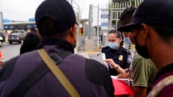 FILE - A U.S. Customs and Border Protection officer examines paperwork of migrants waiting to cross into the United States to begin the asylum process in Tijuana, Mexico, July 5, 2021.