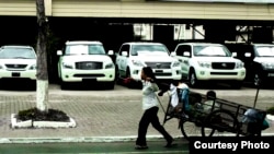 A woman drags a cart with a son inside to collect recycled products to support her daily needs, in front of a row of luxury cars in Phnom Penh, Cambodia. (Photo Courtesy)