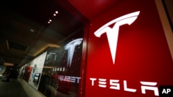 FILE- A sign bearing the company logo is displayed outside a Tesla store in Cherry Creek Mall in Denver, Feb. 9, 2019.