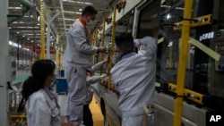 在中國湖北省十堰市的一家工廠，工人為一輛小客車安裝窗板。 (資料照片：2023年5 月10日)