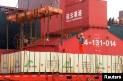 A worker gestures as a crane lifts goods onto a cargo ship, at a port in Lianyungang, Jiangsu province, China, May 31, 2018.