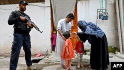 Personel polisi (kiri) berjaga saat seorang petugas kesehatan (kanan) memberikan tetes polio kepada seorang anak selama kampanye vaksinasi polio dari rumah ke rumah di pinggiran kota Peshawar, Pakistan.