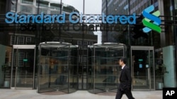FILE - In this Aug 7, 2012, file photo a man walks by Standard Chartered bank in London. British financial services giant Standard Chartered Bank will pay $1.1 billion in fines to settle allegations by U.S. and British authorities that it attempted to eva