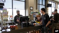 In this photo taken March 20, 2020, Mike Johnston, a clerk at the Maupin Market in tiny Maupin, Oregon, helps a customer while wearing a latex glove to protect himself against the coronavirus.