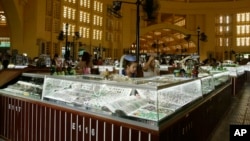 In this Wednesday, Feb. 27, 2013, Cambodian vendors sit in their jewelry booths in the Central Market (Phsar Thum They) in Phnom Penh, Cambodia. Beneath a lemon-yellow art deco dome, the Central Market offers miles of no-strings-attached window-shopping.