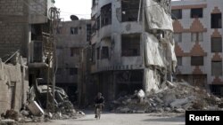 Un homme passe, à vélo, devant des bâtiments endommagés dans le quartier de Douma, à Damas, Syrie, 26 novembre 2015.
