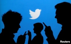 FILE - People holding mobile phones are silhouetted against a backdrop projected with the Twitter logo, Sept. 27, 2013.