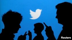 FILE - In this illustration photo, people holding mobile phones are silhouetted against a backdrop with the Twitter logo, Sept. 27, 2013. 