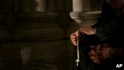 FILE - A member of the clergy prays the rosary as he waits for Pope Francis to arrive at St. Patrick's Cathedral for evening prayer service in New York, Sept. 24, 2015. Across the U.S., Catholics once faithful with their financial support to their churche