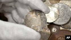 In this Sept. 9, 2021 photo provided by auctioneer Morton & Eden Ltd., a rare 17th century one shilling coin is displayed above a metal box containing other coins, at the auction house, in London.