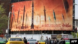 Automovilistas y peatones en Teherán circulan por delante de un cartel que muestra misiles balísticos iraníes con un texto en árabe que dice: "la promesa [de la persona] honesta" y en persa: "Israel es más débil que una telaraña", en la plaza Valiasr el 15 de abril de 2024.