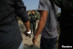 A U.S. border patrol agent stands next to men being detained after entering the United States by crossing the Rio Grande river from Mexico, in Roma, Texas, May 11, 2017. Some Republicans would like to tie DACA to the larger issues of border control and a resolution of the status of the nearly 12 million undocumented people now living in the United States.