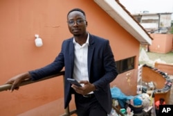 Shadrach Damateye, a co-founder of Masters Hive Center for Innovation, who uses his mobile phone to help business owners, poses for a photograph outside his office in Tema, Ghana, Tuesday, April 23, 2024. (AP Photo/Misper Apawu)