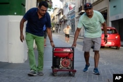 FILE - Men push a generator along Fortaleza street, one month after Hurricane Maria, in San Juan, Puerto Rico, Oct. 20, 2017.