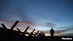 FILE - A U.S. border patrol agent walks along the border fence separating Mexico from the United States near Calexico, California, Feb. 8, 2017. 