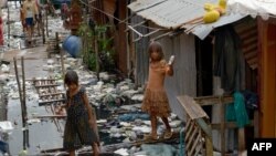 រូបឯកសារ៖ កុមារពីរនាក់ដើរជាន់លើក្តារពីលើទឹកស្អុយនៅតំបន់មួយ​ក្នុង​រាជធានីភ្នំពេញ កាល​ពីថ្ងៃទី១៨ ខែតុលា ឆ្នាំ២០១៧។ 