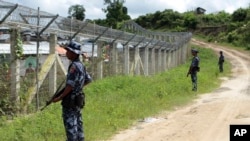 မြန်မာ-ဘင်္ဂလားဒေ့ရှ် နှစ်နိုင်ငံနယ်စပ်အကြားရှိ "no man's land" ကိုကာရံထားသည့် ခြံစည်းရိုးနားတွင် လုံခြုံရေးတာဝန်ယူထားသည့် မြန်မာ နယ်ခြားစောင့် တပ်ဖွဲ့ဝင်များ။ (တောင်ပြိုလက်ယာကျေးရွာအနီး၊ မောင်တောမြို့) (ဇွန် ၂၉၊ ၂၀၁၈)