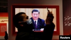 A visitor holds his mobile phone near a screen showing Chinese President Xi Jinping