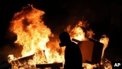 A masked anti-government protester stands by a burning street barricade in Santiago, Chile, Oct. 28, 2019. 