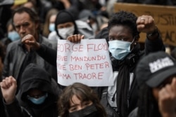 FILE - A man holds a placard reading "George Floyd, Herve Mandundu, Mike Ben Peter and Adama Traore" during a protest against racism and police brutality in Lausanne, France,  June 7, 2020.